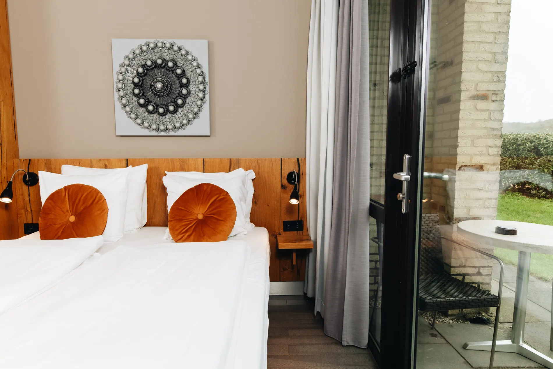 Sfeervolle hotelkamer met een glazen deur die direct toegang biedt tot een privéterras met buitenmeubilair en uitzicht op het groen.